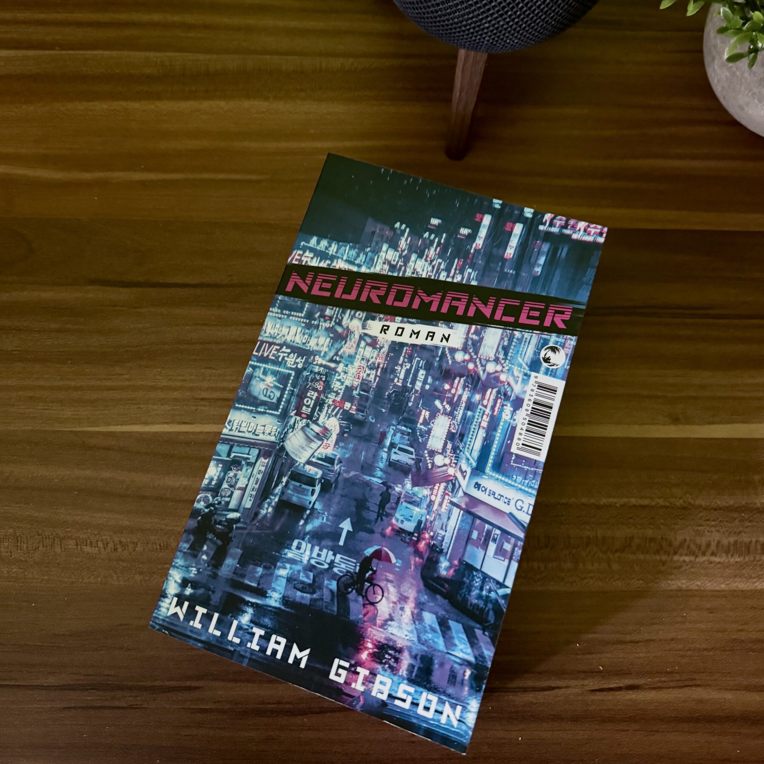 Das Buch „Neuromancer“ von William Gibson liegt auf meinem Nachttisch. Auf dem Cover ist eine futuristische, nächtliche Großstadt mit beleuchteten Reklametafeln und regennassen Straßen zu sehen.